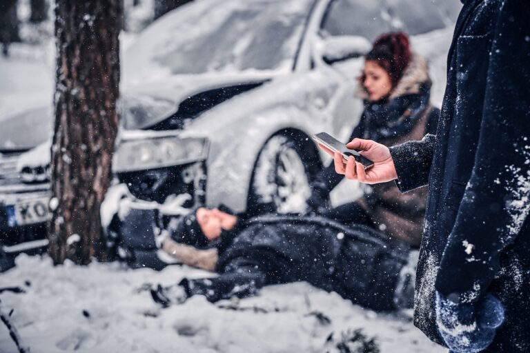 A person in a winter coat using a smartphone to document the accident scene and call for help, following the steps after a car wreck in snowy conditions.