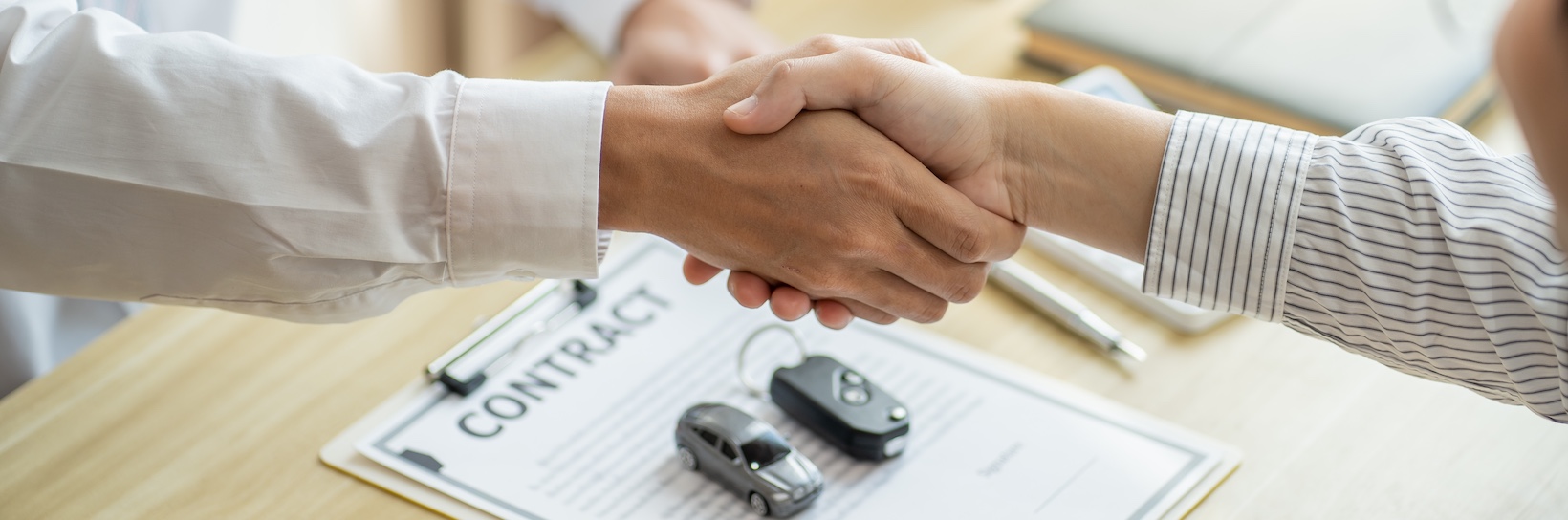 Two men are shaking hands over a vehicle contract, a toy car, and keys, demonstrating that understanding your rights leads to fair settlements.